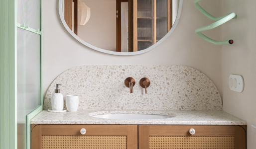 Nowoczesna łazienka z blatem terrazzo, plecioną drewnianą szafką i nieregularnym lustrem