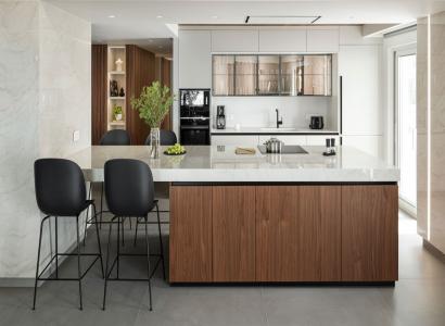 Nowoczesna kuchnia z wyspą wykończoną płytkami wielkoformatowymi imitującymi marmur, z frontami z drewna i blatami o wysokim połysku