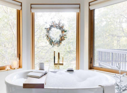 Świąteczna aranżacja łazienki z wolnostojącą wanną i złotą baterią wannową przy oknie